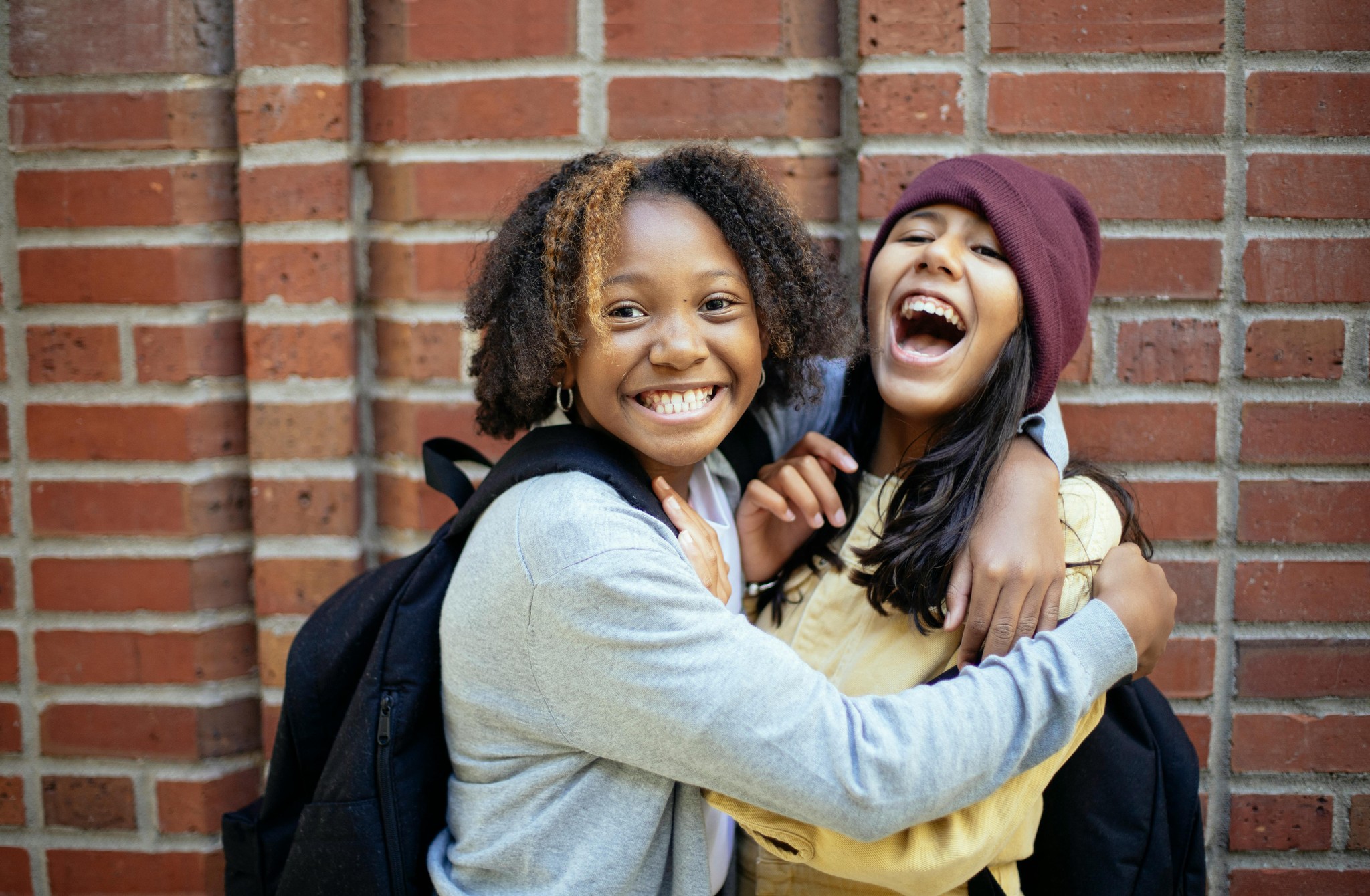 Two smiling students leaning against a brick wall